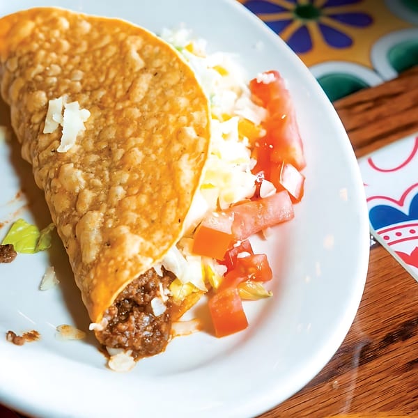 A crispy taco filled with ground beef, lettuce, cheese, and diced tomatoes on a white plate.